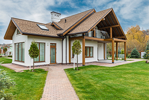A modern two-story white house with a tan shingle roof and wooden accents features large glass windows and a manicured green lawn